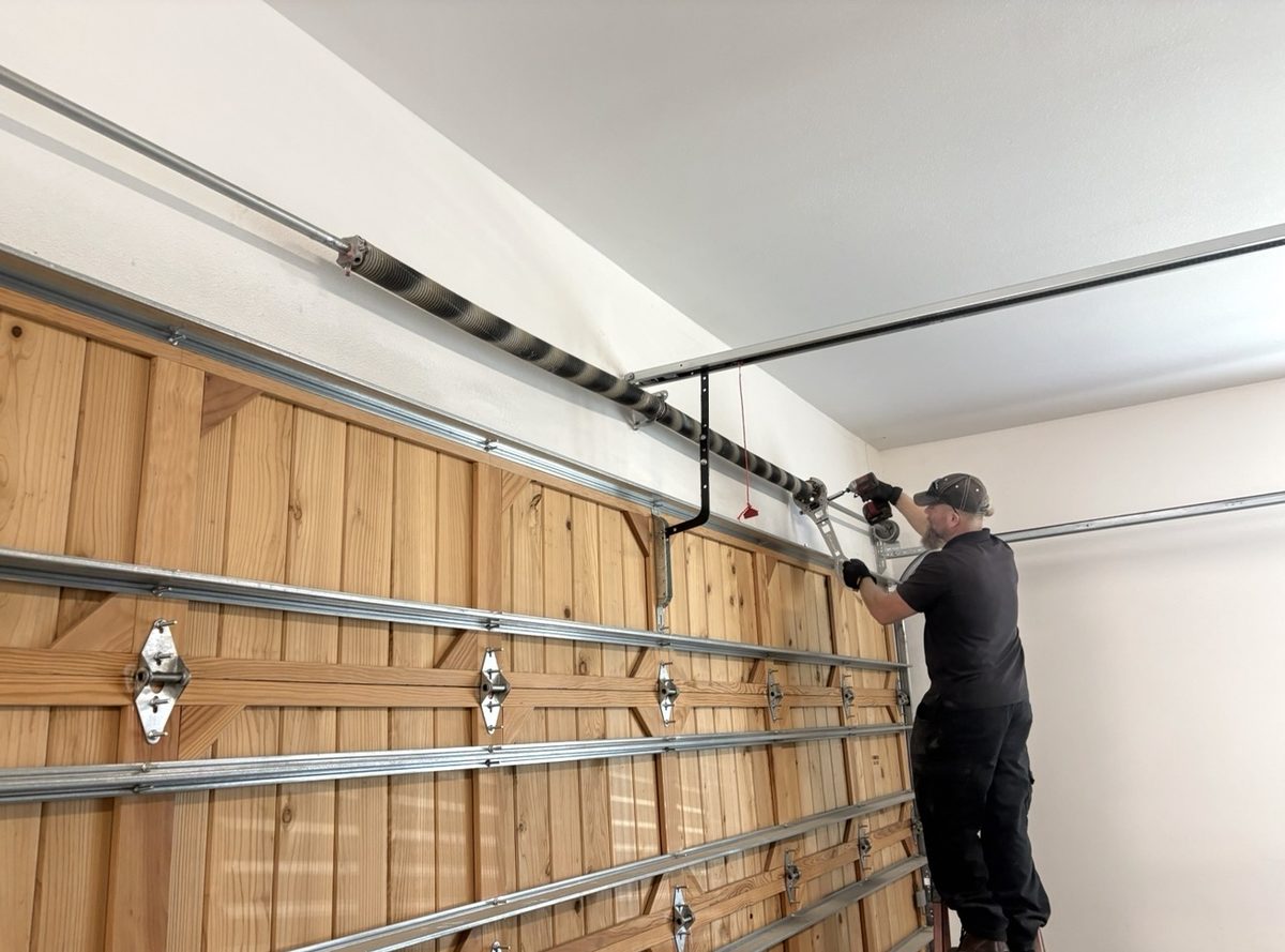 Technician winding a replacement torsion spring above a cedar garage door